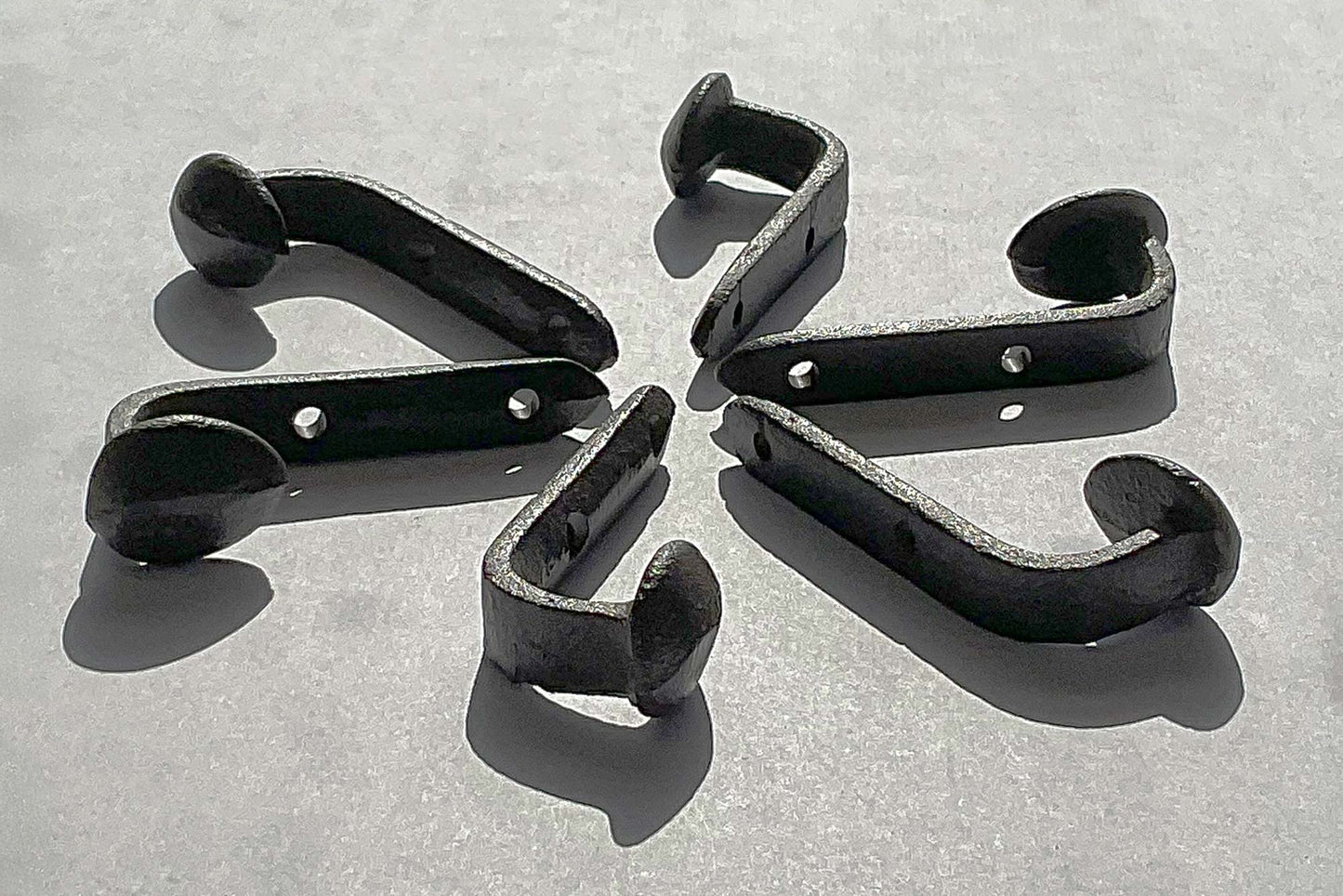Side view of a cast iron railroad tie hook showing 2.25 inch depth from wall to spike head laid in a circle in the bright sunlight so you can clearly see the hook from all angles and the metal texture