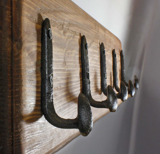 Close-up of antique-style blacksmith finish on a western-style metal wall hook with mounting screws. Five railroad spike hooks arranged in a row on a DIY wooden towel rack for a bathroom.