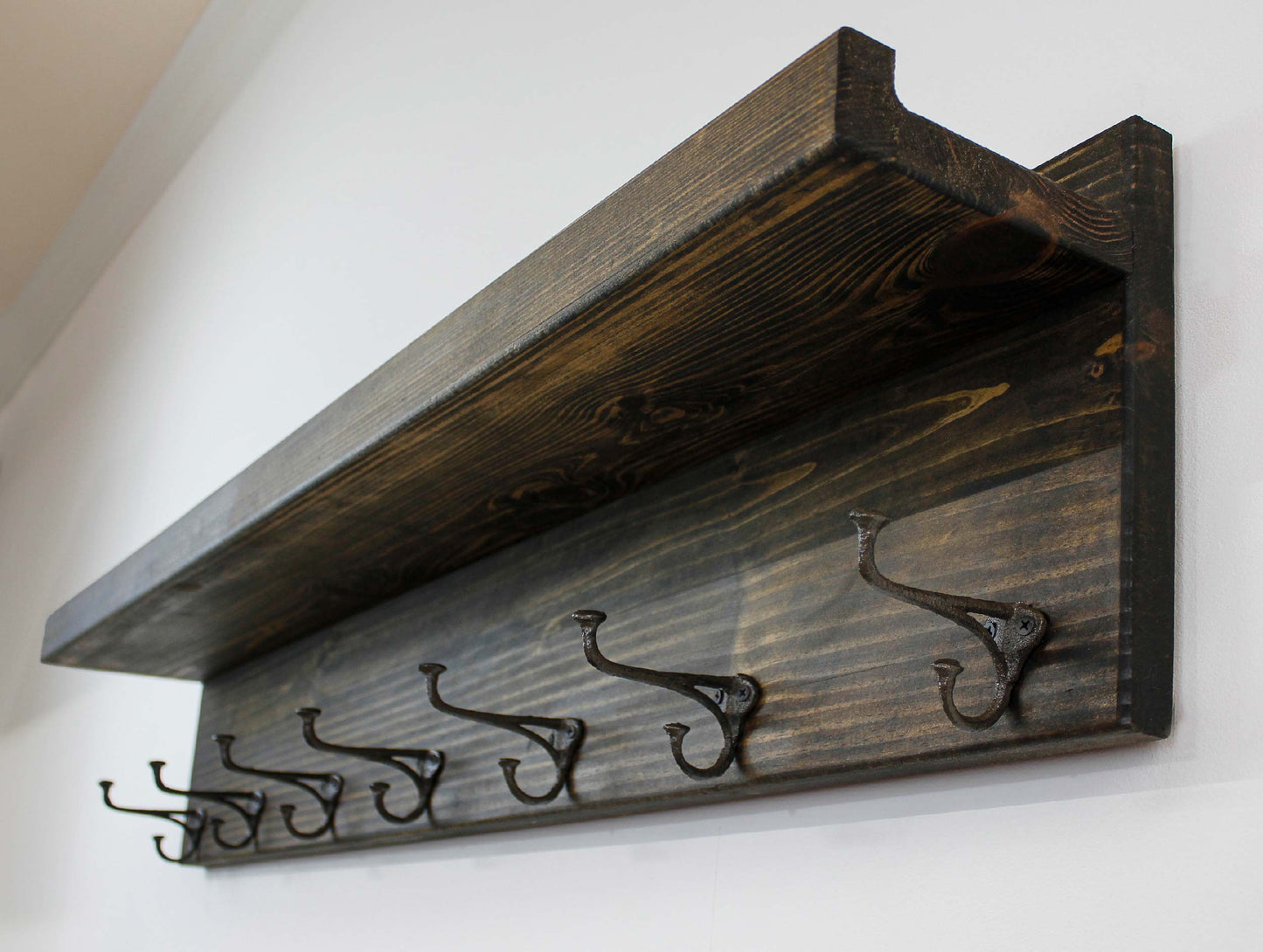 May include: A rustic wooden coat rack with three dark metal hooks. The rack has a shelf and is stained in a warm brown color, showcasing the wood grain. The hooks are ornate and add a vintage touch to the entryway decor.