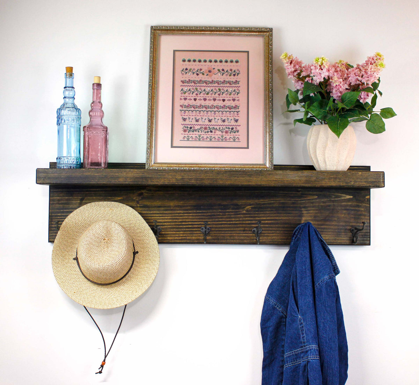 Wooden shelf with coat hooks, hat, and decorative items on a white wall.