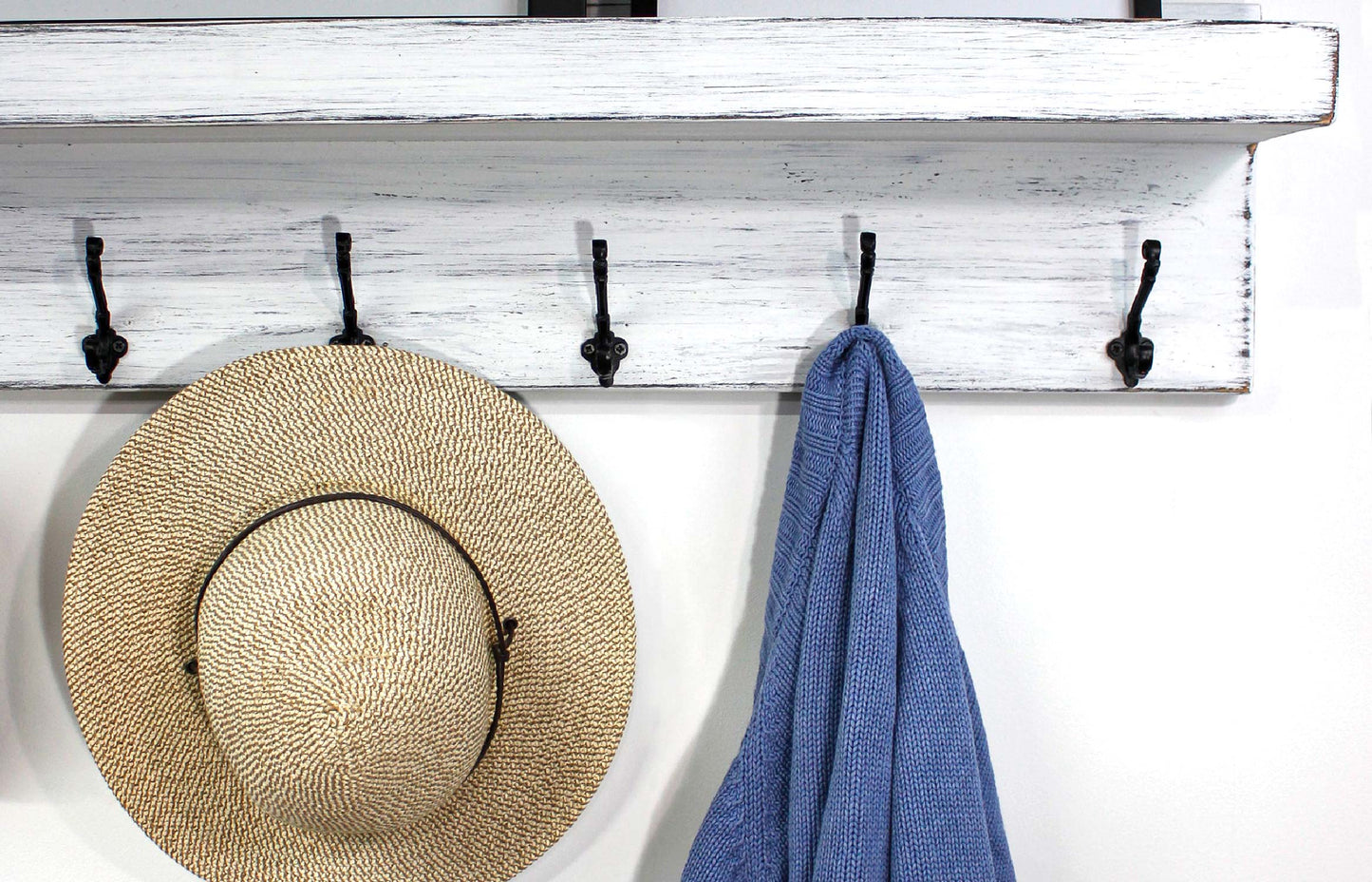 closeup of clothing and hat hung on the black metal hooks on a picture ledge coat rack