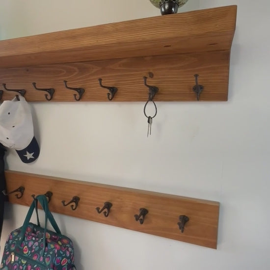 rustic coat rack with  dark metal hooks mounted on a stained wooden board. The nailhead vintage hooks have a curved design and are attached with screws. The wood grain is visible, adding to the natural aesthetic.