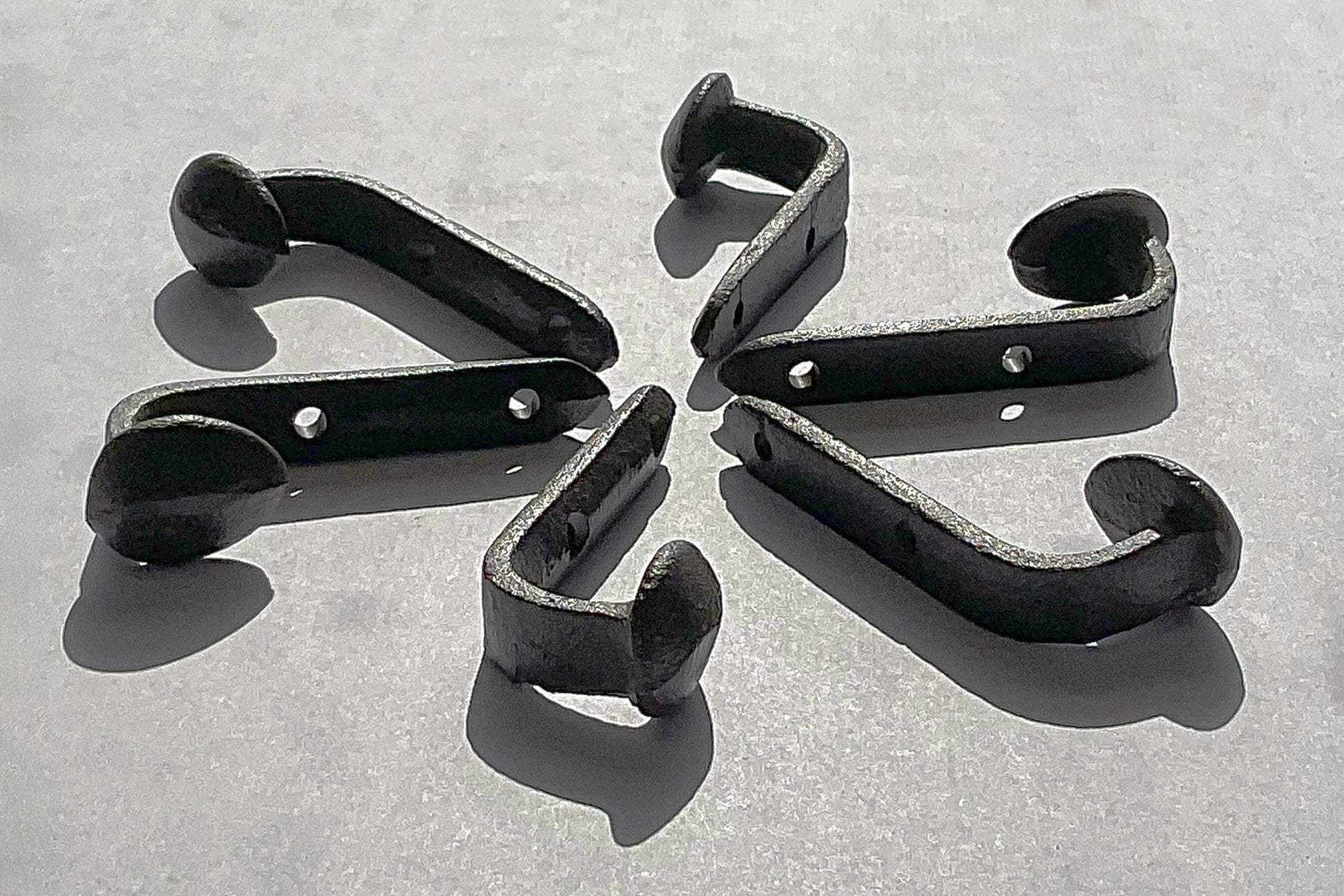 Side view of a cast iron railroad tie hook showing 2.25 inch depth from wall to spike head laid in a circle in the bright sunlight so you can clearly see the hook from all angles and the metal texture