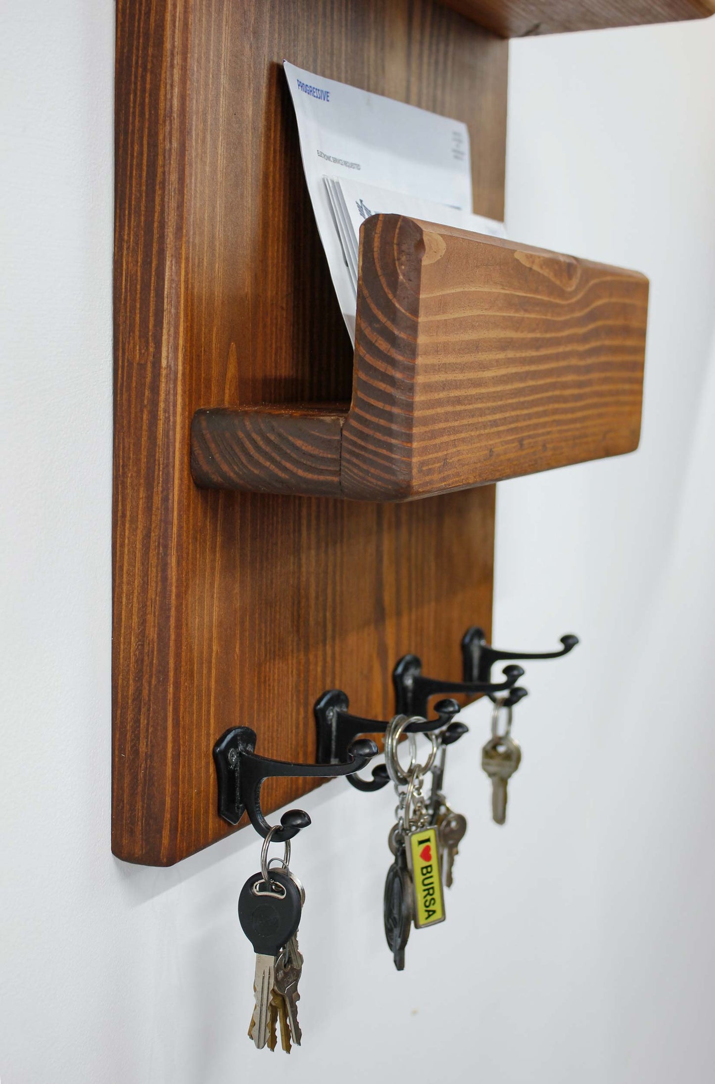 closeup of the small black double hooks that hold keys, leashes, straps and handles of small items | see the mail storage shelf with a wooden front lip to conveniently hold letters by the front door | the top features two shelves one with a short lip for a small picture ledge to hold holiday decor, small plants, pictures, welcome decor, blackboard, notes for people as they enter or exit a home or business | the warm stained wood has an inviting rustic friendly vibe as well as being functional